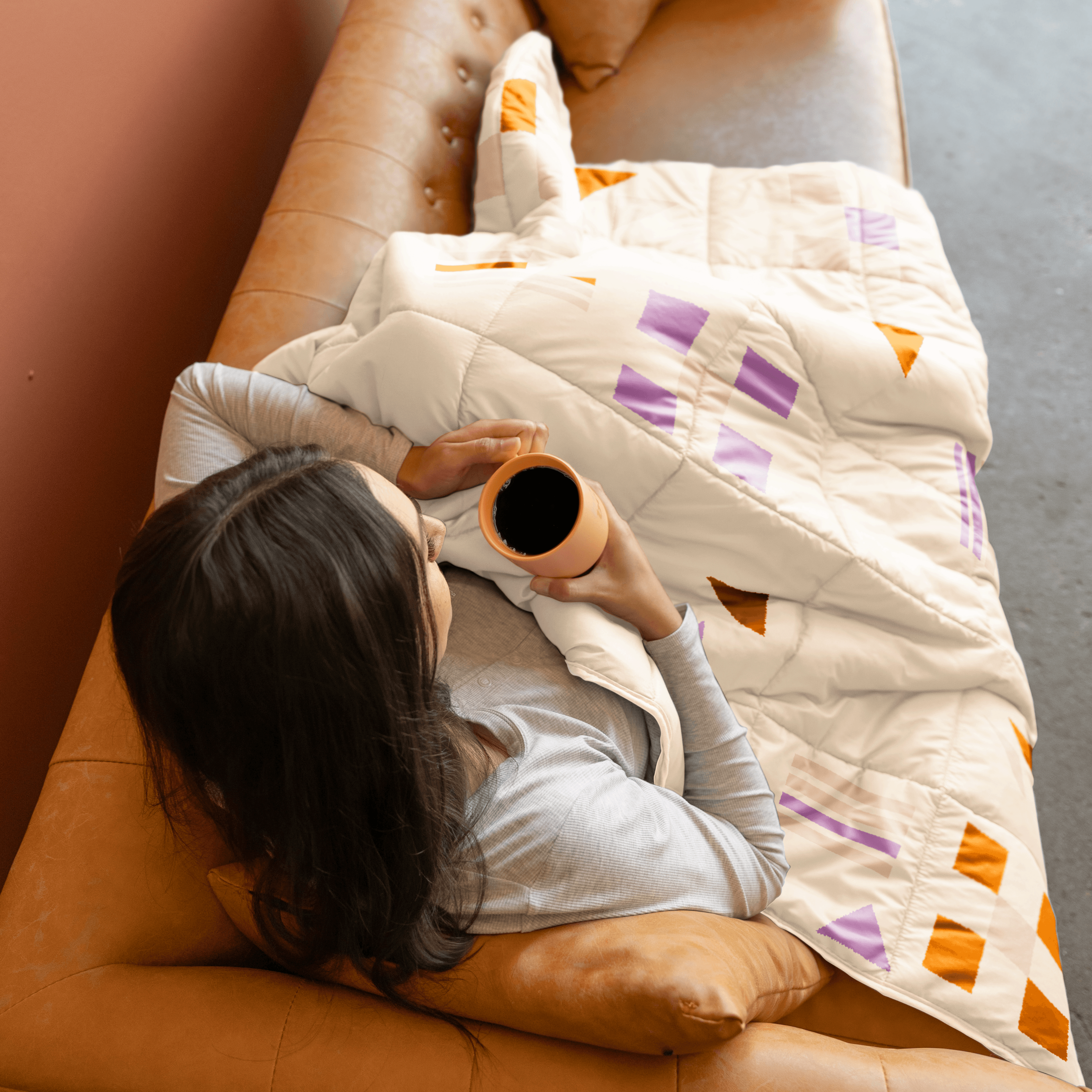 an arial shot of someone on a couch holding a cup of coffee with the soft block blanket on their lap.