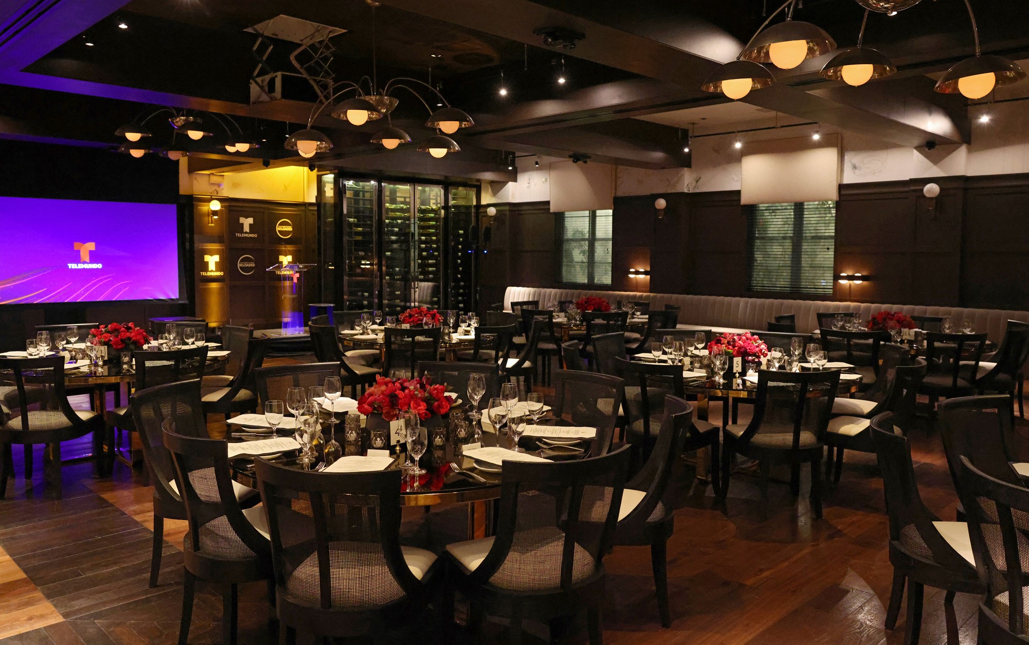 Private dining room set for a corporate dinner with round tables, floral centerpieces, and presentation screen.