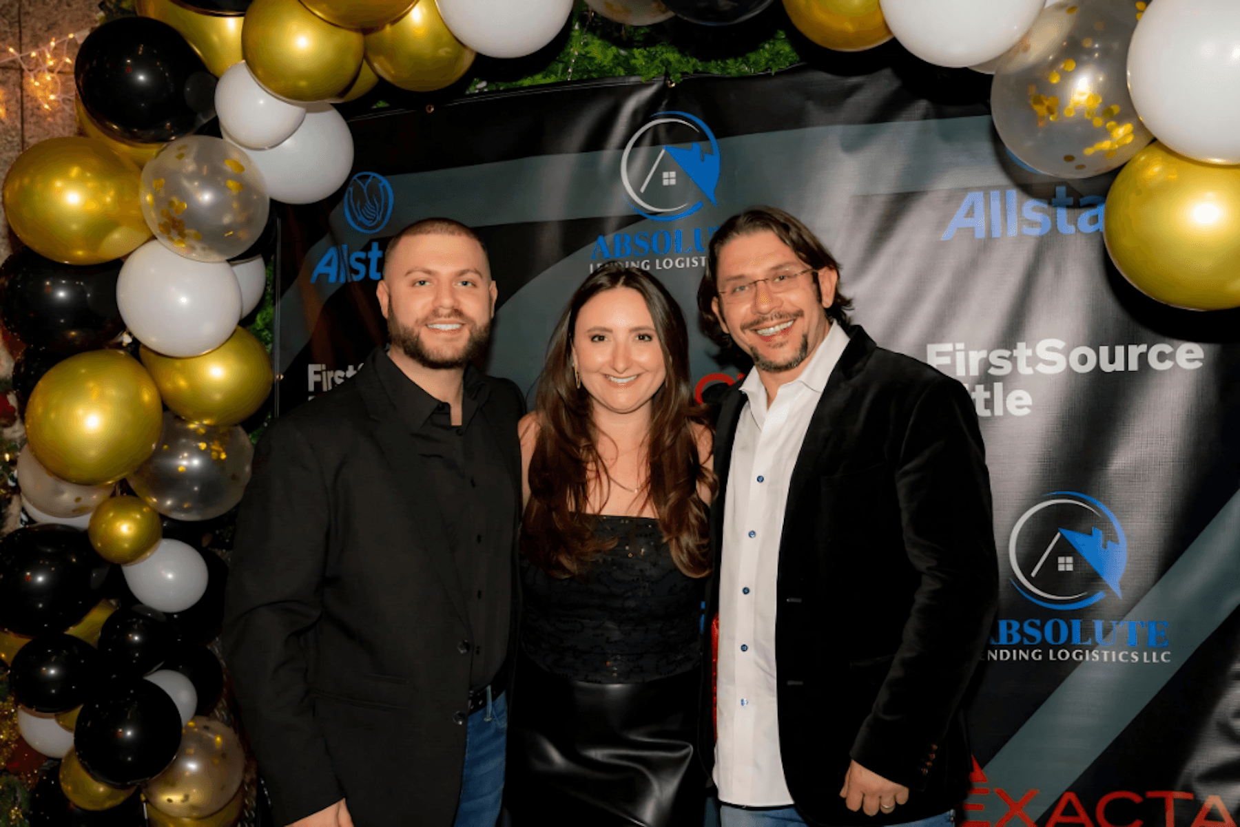Stas Tsiperson with colleagues at a networking event, standing before sponsor backdrop and balloon display.