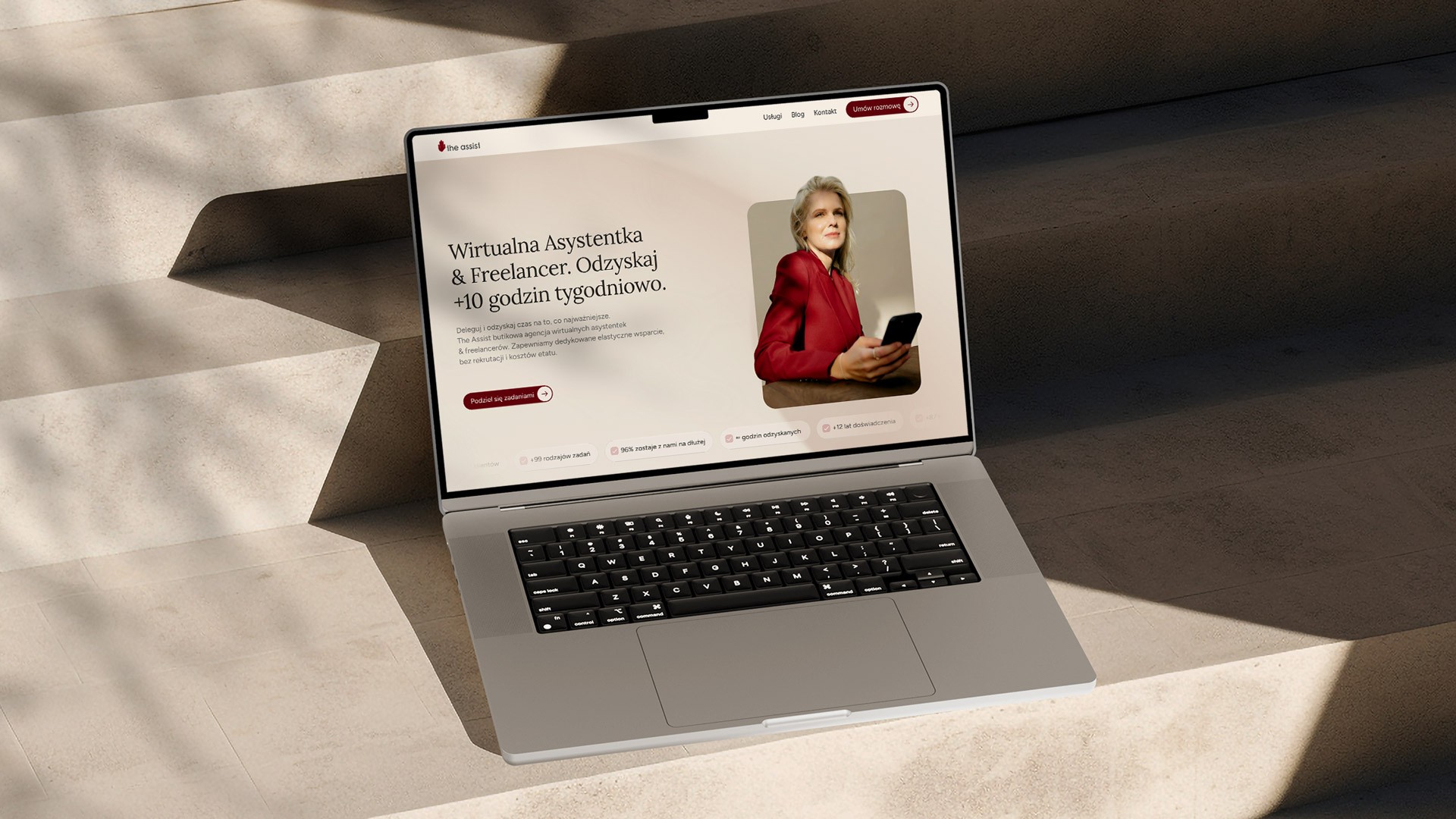 Mockup strony internetowej The Assist dla wirtualnej asystentki i freelancera, prezentowany na laptopie ustawionym na betonowych schodach.