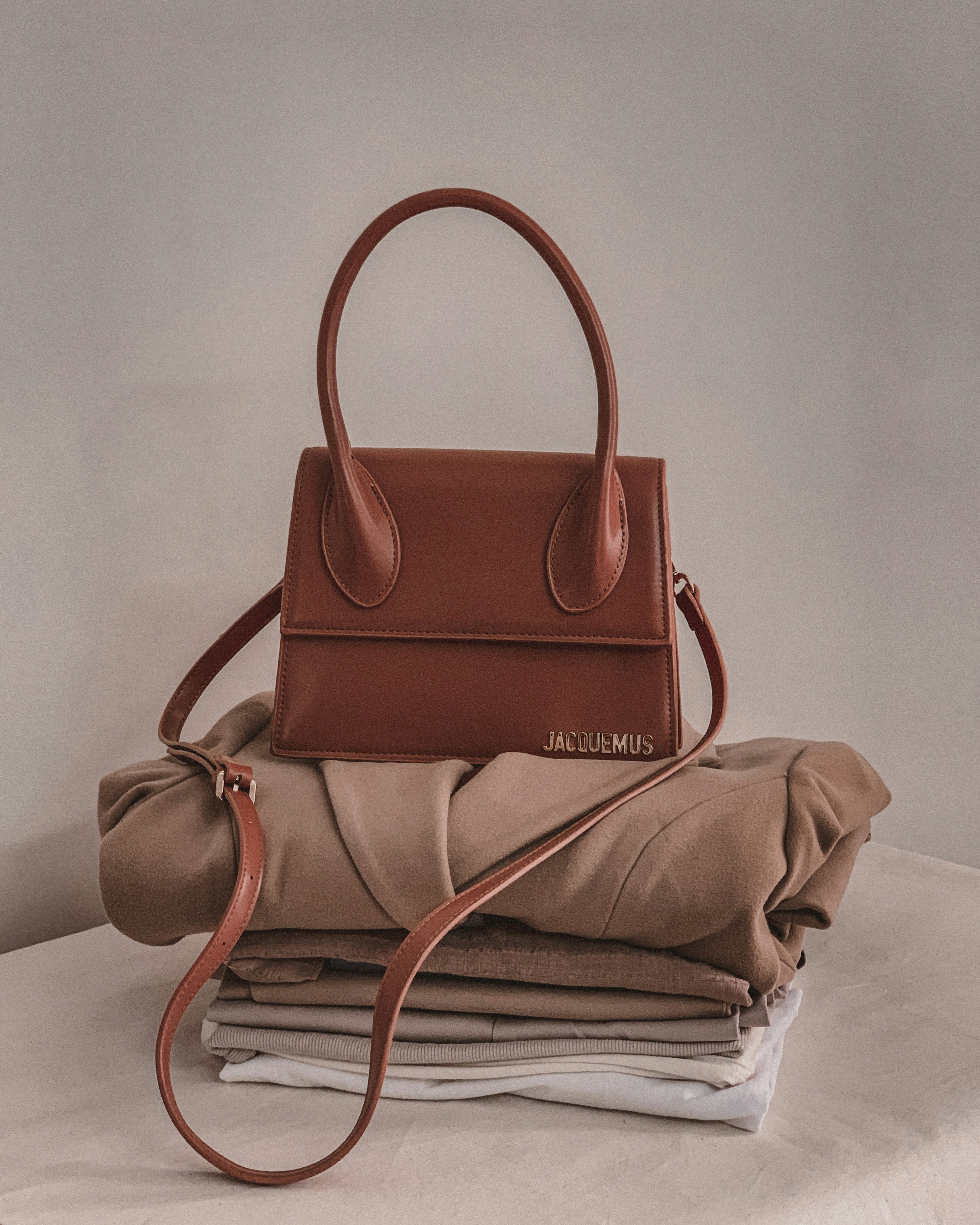 a brown purse sitting on top of a pile of folded clothes