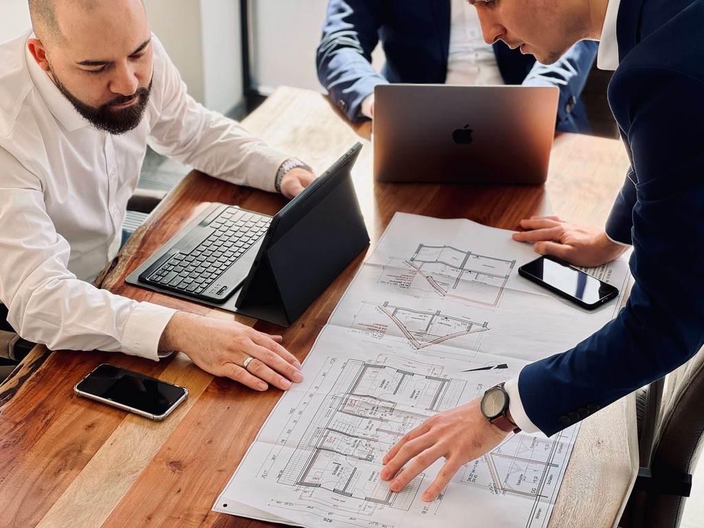 Two people collaborating over a project plan on a table, with laptops and documents visible.