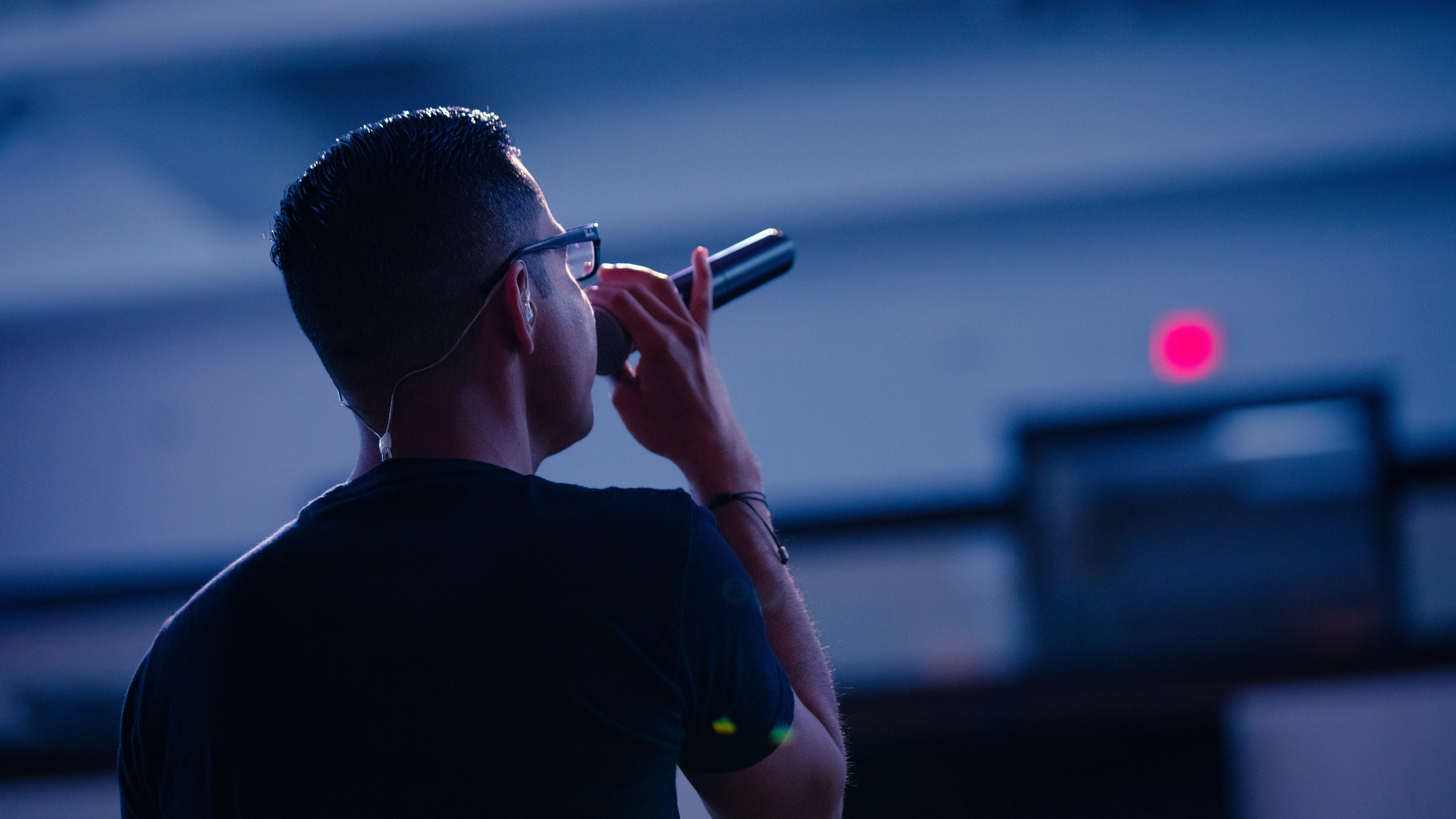 Male singer in black crew neck shirt with his back turned singing into a mic in a room. Photo by Matthew Ball on Unsplash    