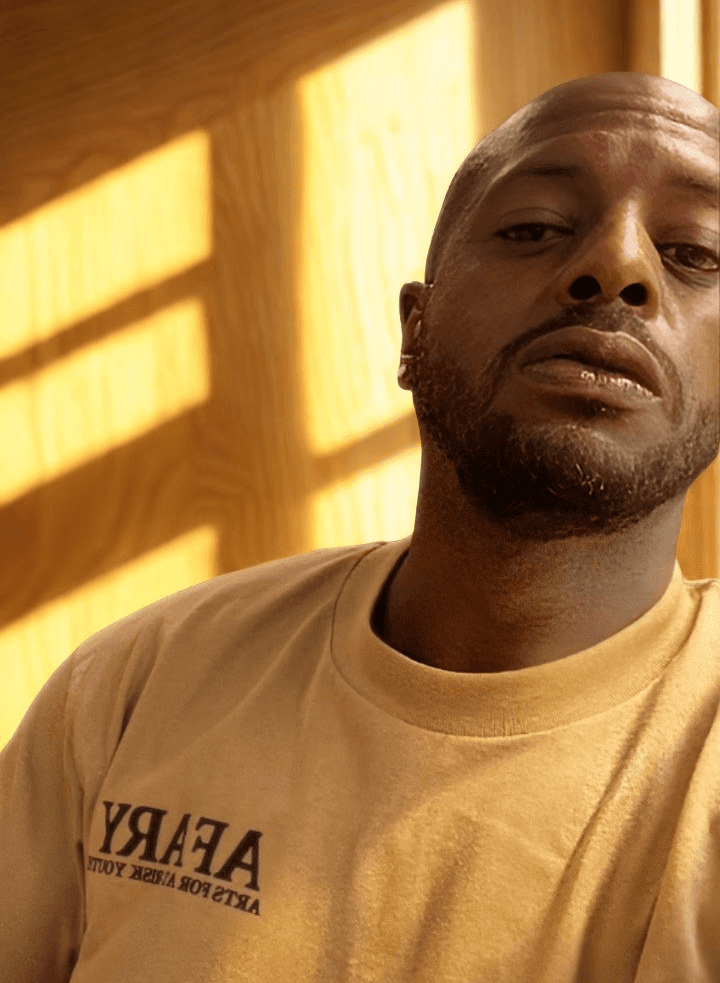 Smiling woman in beige yoga outfit sitting in natural light with green plants in the background.