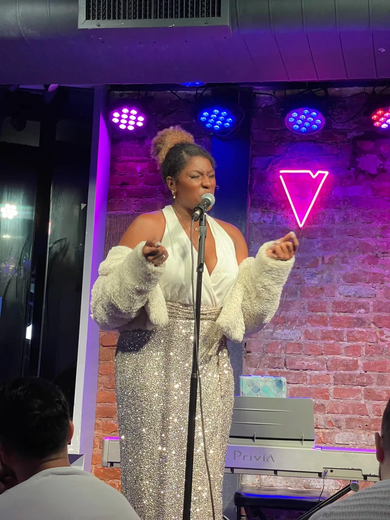 A performer opens both arms wide against the brick back wall