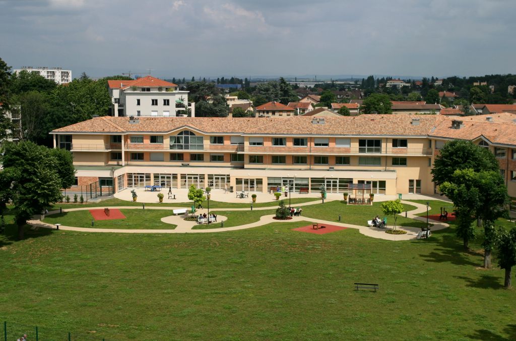 Psychiatric clinic facility with warm terracotta-toned facade, large manicured lawn, landscaped gardens, and tree-lined surroundings