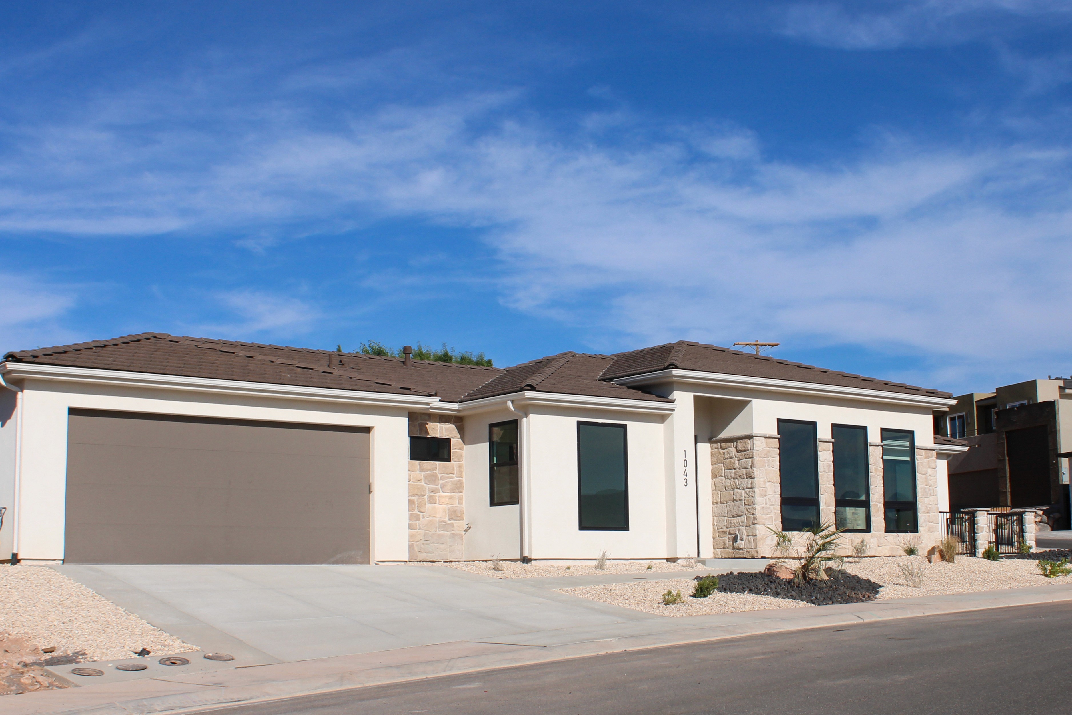 Side exterior of The Overlook at Falcon Ridge in Hurricane, Utah, showing driveway, garage, and stone and stucco accents.