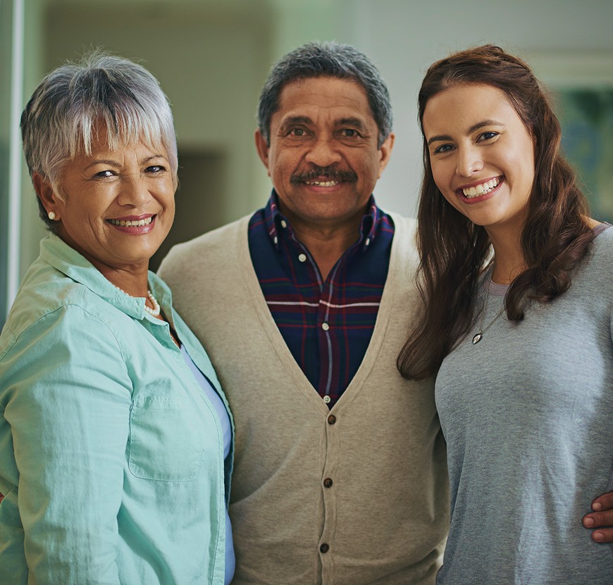 A close-up portrait of three smiling people across three generations: an older woman with silver hair, an older man, and a young adult woman
