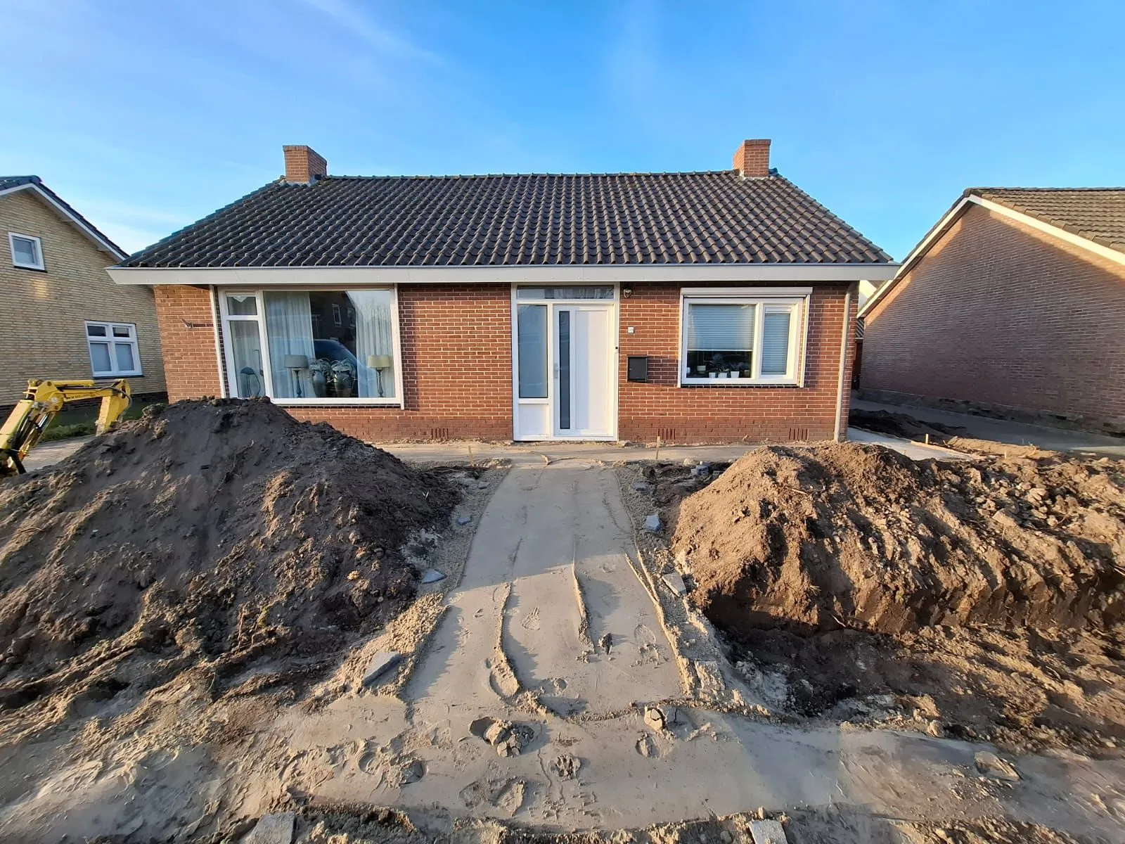 Voortuin in Harkema in renovatiefase met opgehoogde aarde en vrijstaand bakstenen huis met wit kozijn.