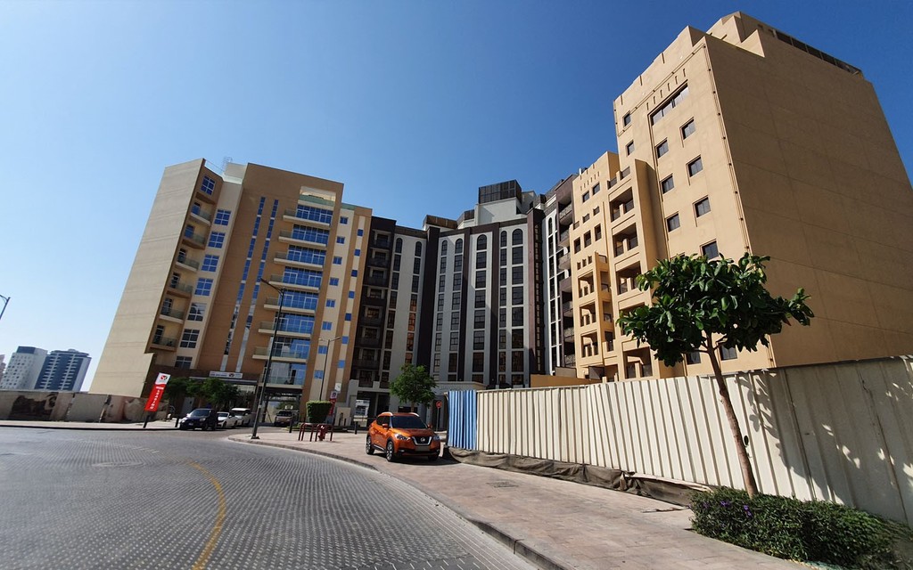 Orange car parked on sunny street in Al Jaddaf, Dubai, with modern mid-rise buildings and active urban development.