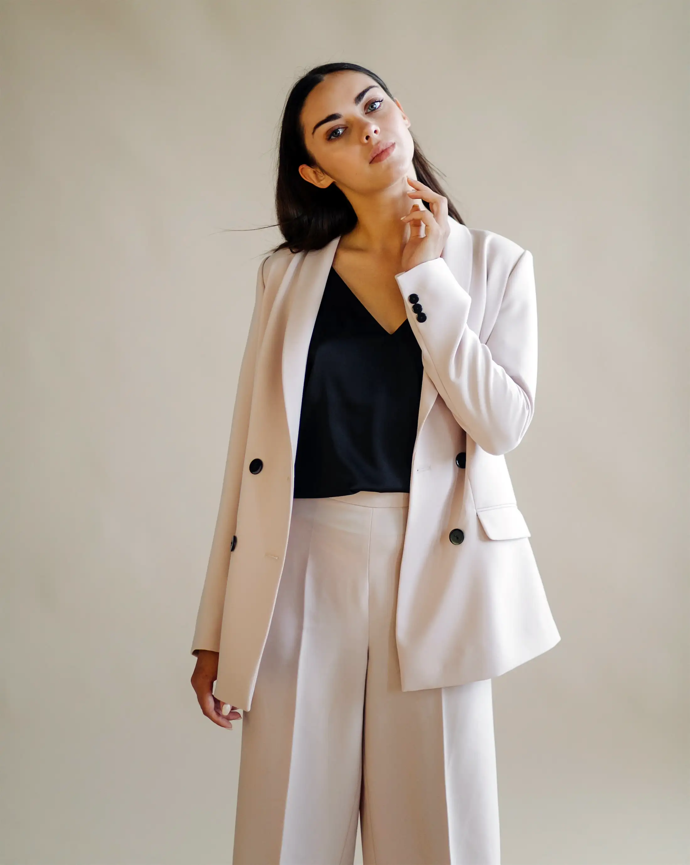 Model in a blush double-breasted trouser suit over a black top against a neutral studio backdrop