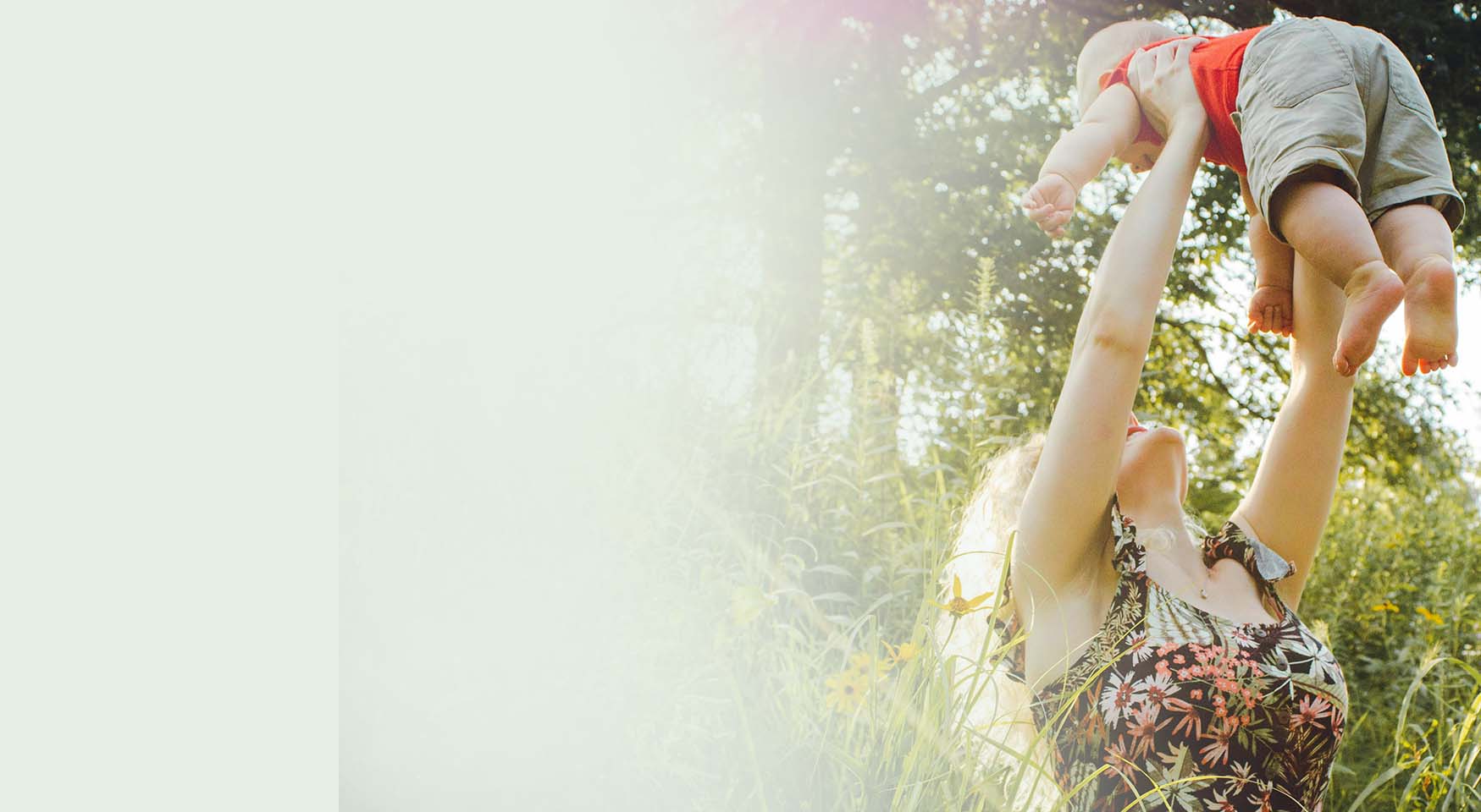 Woman gently throwing her happy baby in the air in a grass field