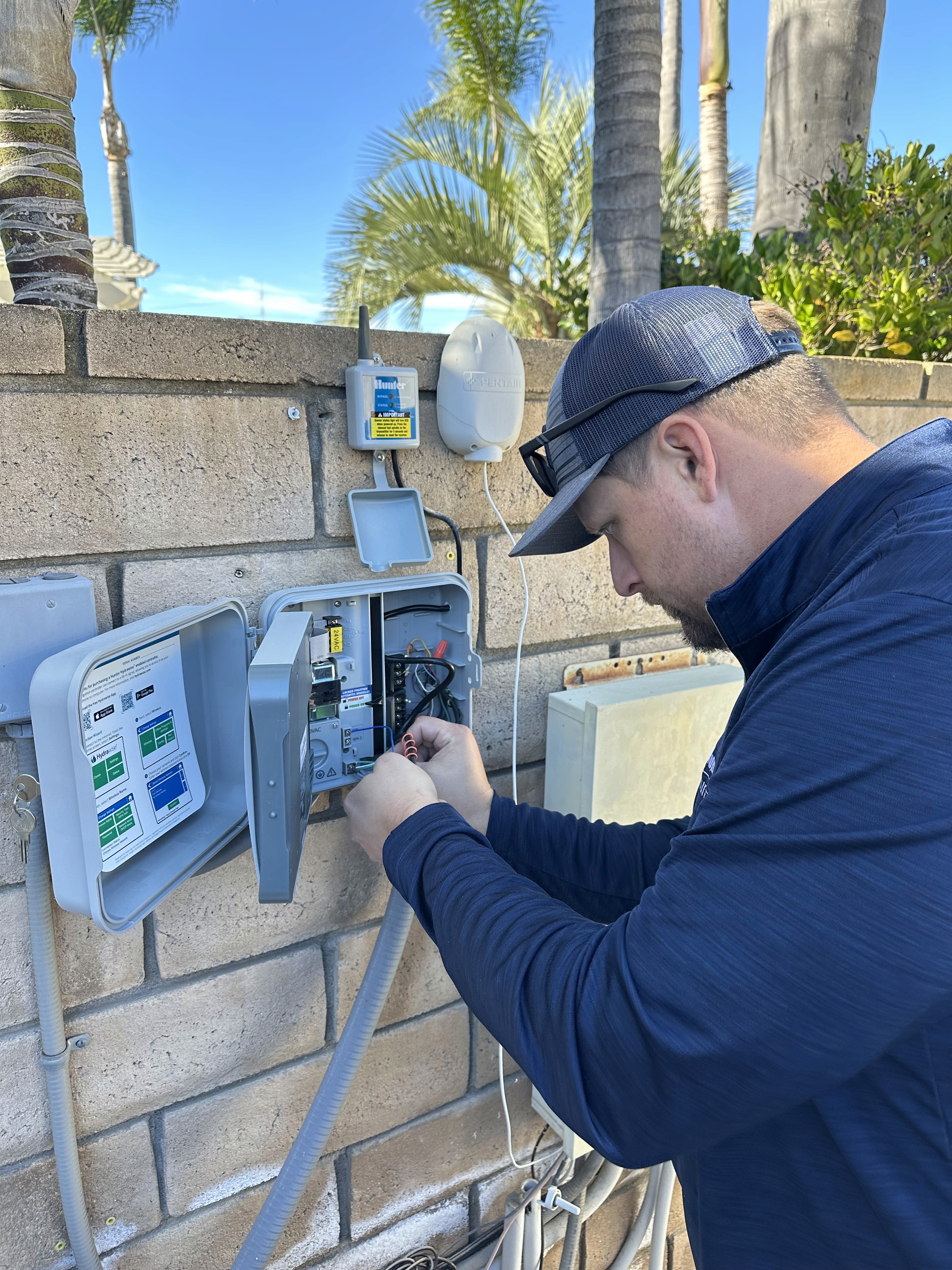 Professional technician performing sprinkler system repairs on a wall-mounted irrigation controller.