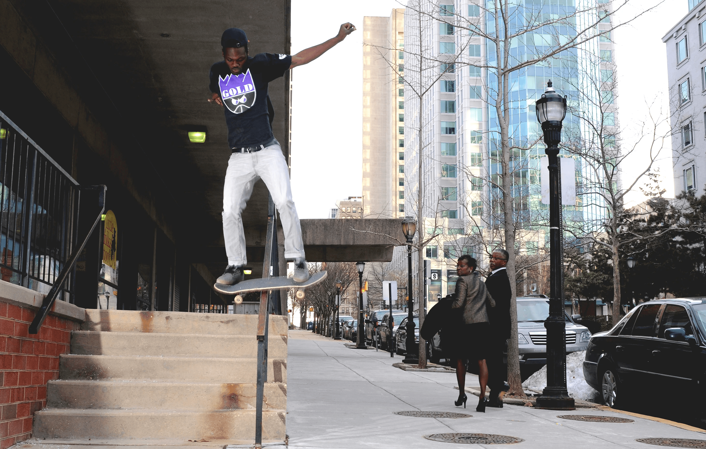 Digital photography of a skateboarder on a city stair handrail as passersby watch him mid-trick
