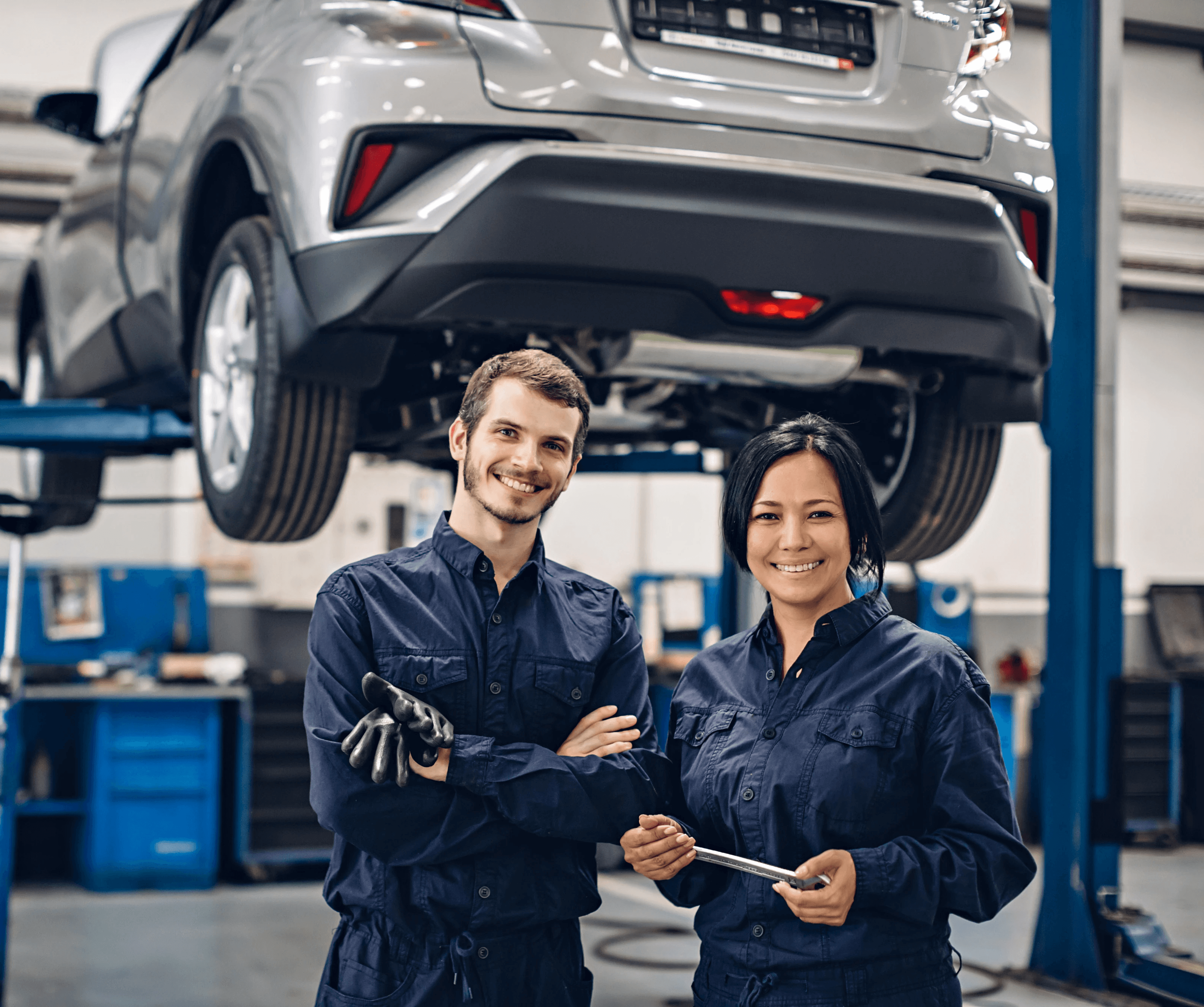 two mechanics standing in an auto shop with car and equipment in background