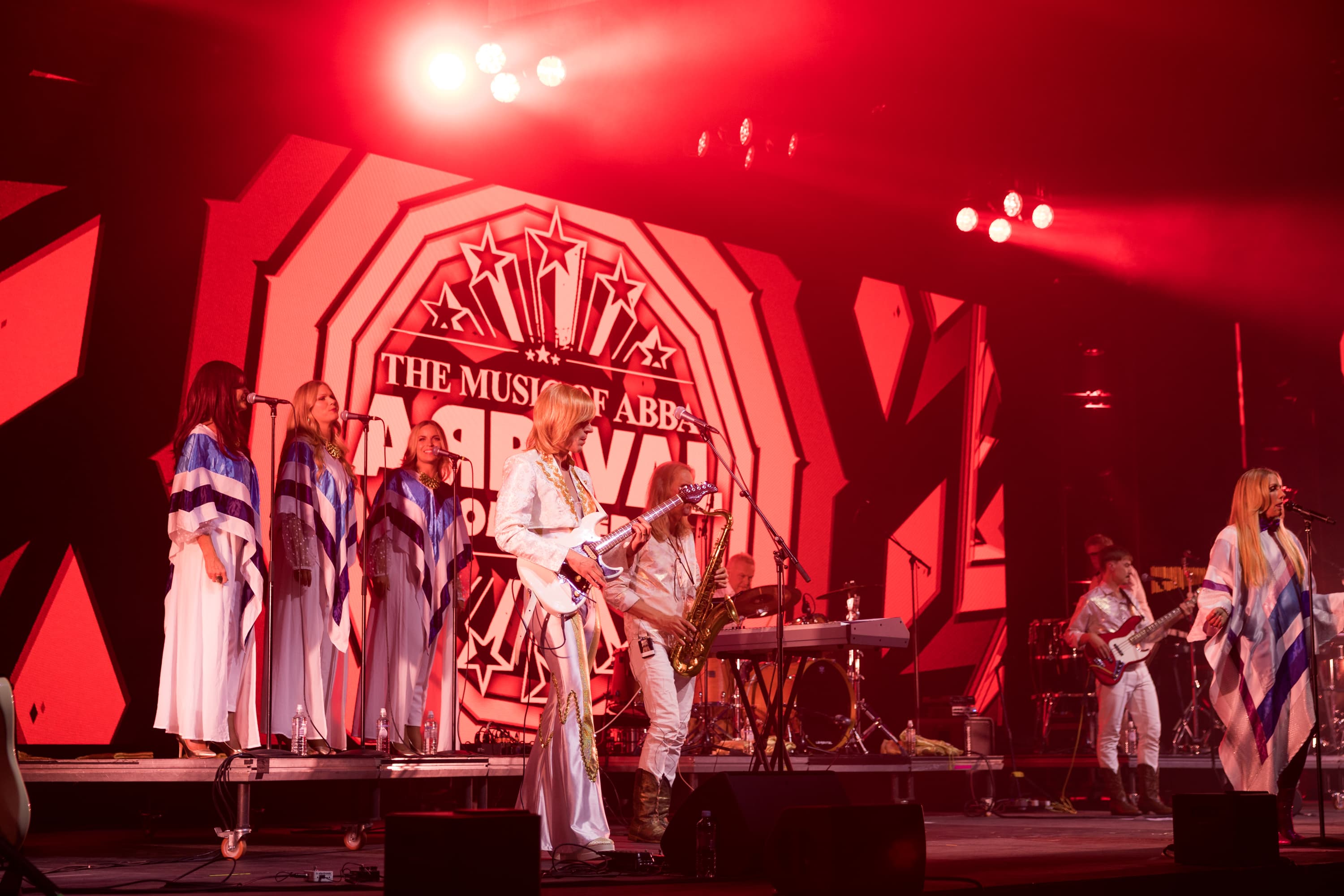 musicians standing on a red lit stage in 70's outfits