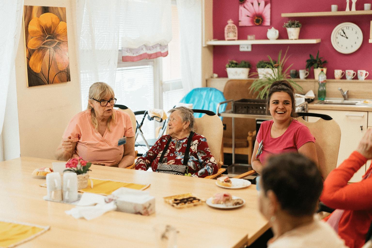 Residents and staff sitting round the table with cake in a care home dining room.