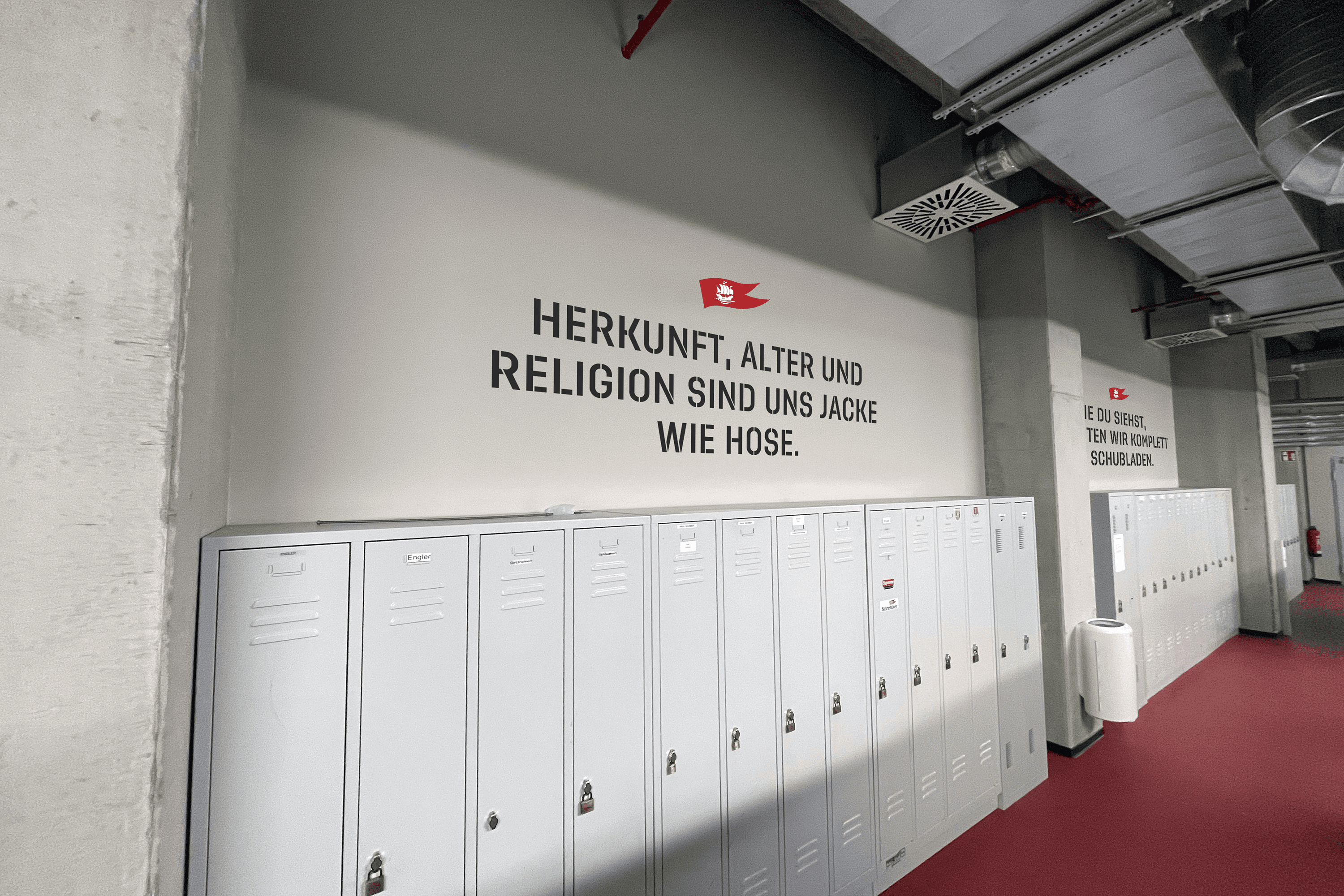 Lockers with text on wall saying "HERKUNFT, ALTER UND RELIGION SIND UNS JACKE WIE HOSE."