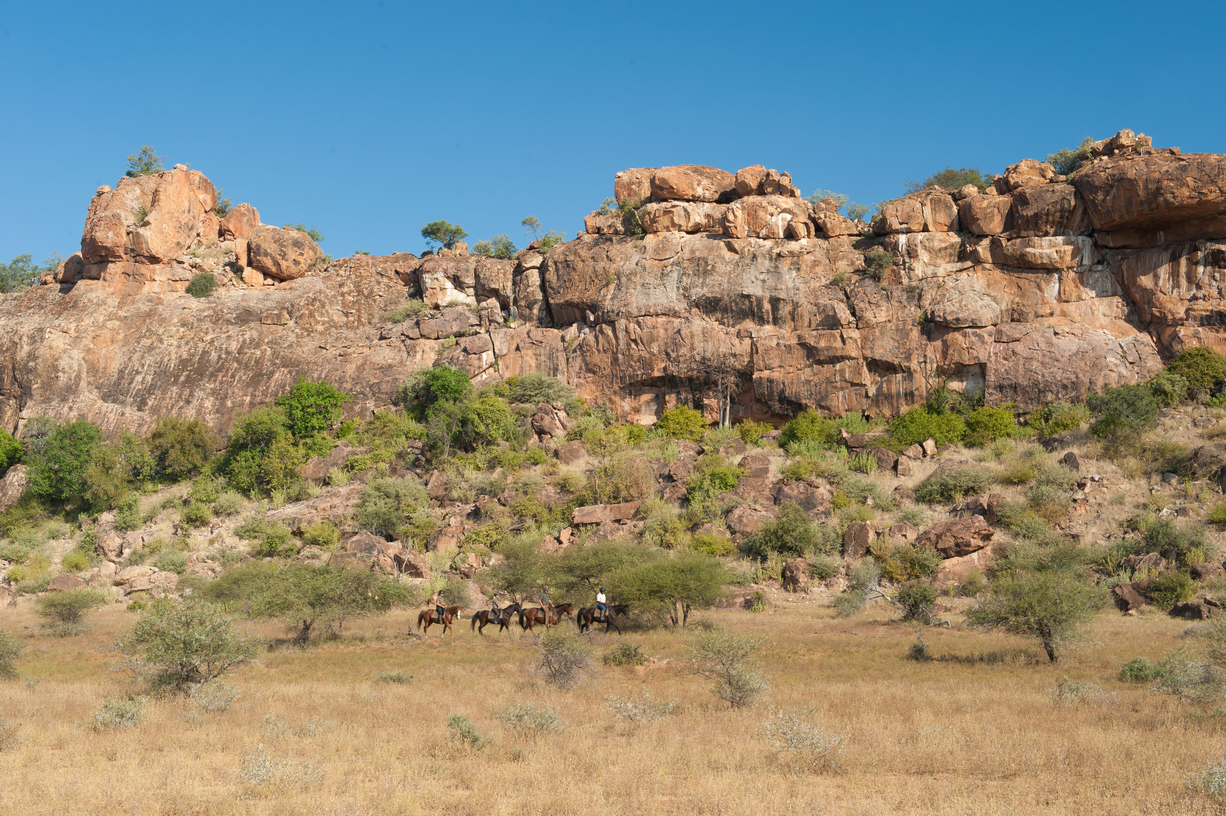 Tuli Safari, Botswana. Ryttare galopperar längs en mäktig sandstensvägg – dramatisk natur och frihetskänsla under ridsafari i Mashatu.