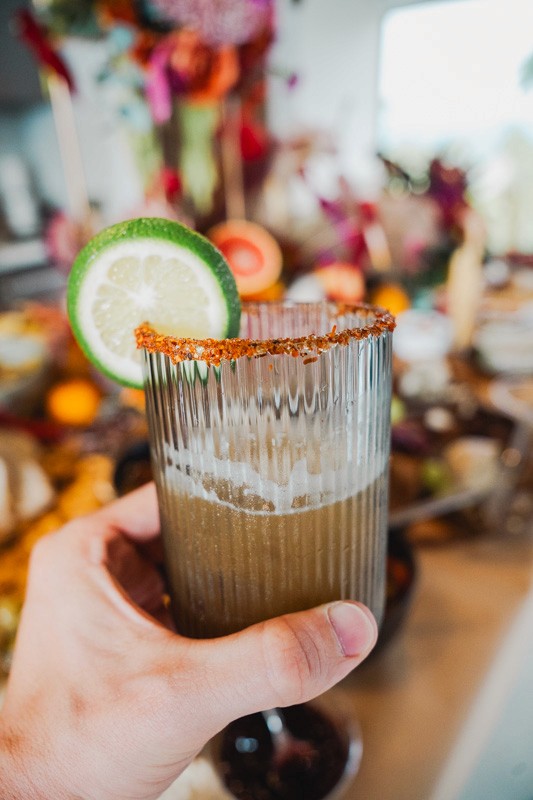 Close-up of a tropical cocktail with a chili rim and lime served alongside a gourmet grazing table.