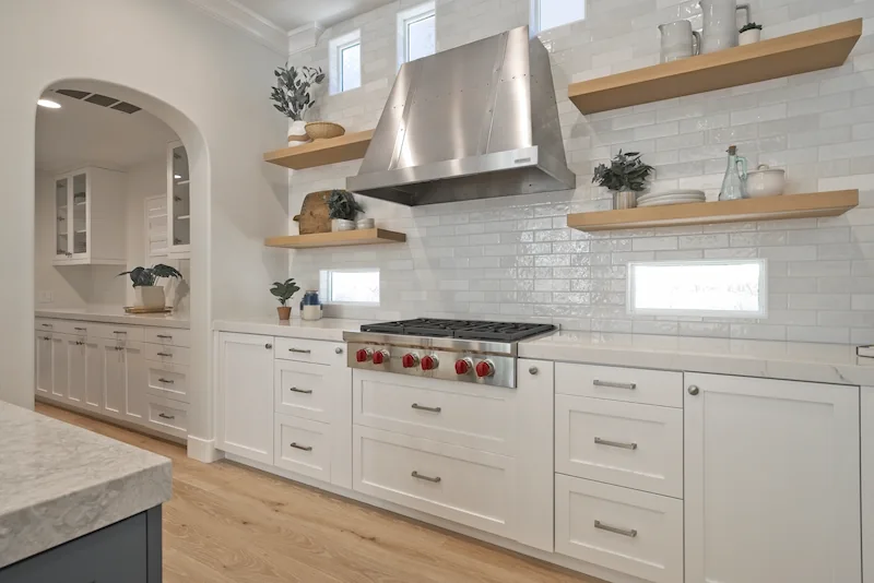 Elegant kitchen with white cabinetry, wooden shelves, and professional range in Bonita Canyon Remodel.