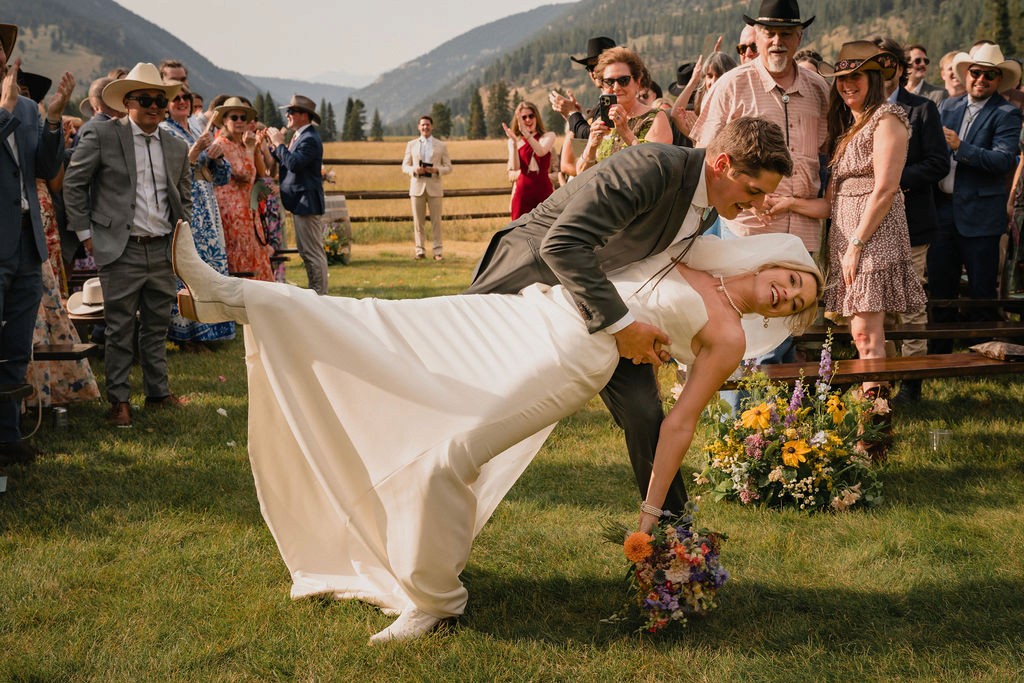 One newlywed dipping the other beside a rustic fence