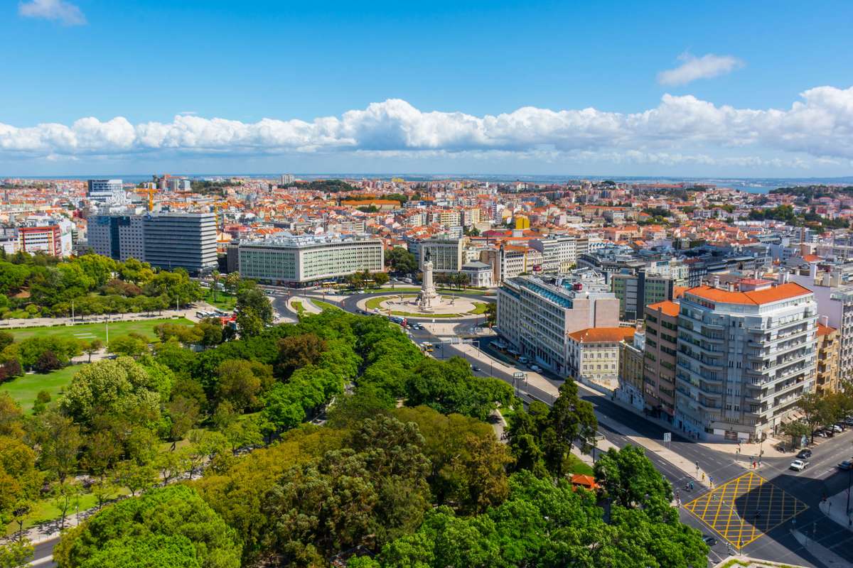 High-angle view of a city skyline with a large park and green trees in the foreground under a blue sky with clouds.