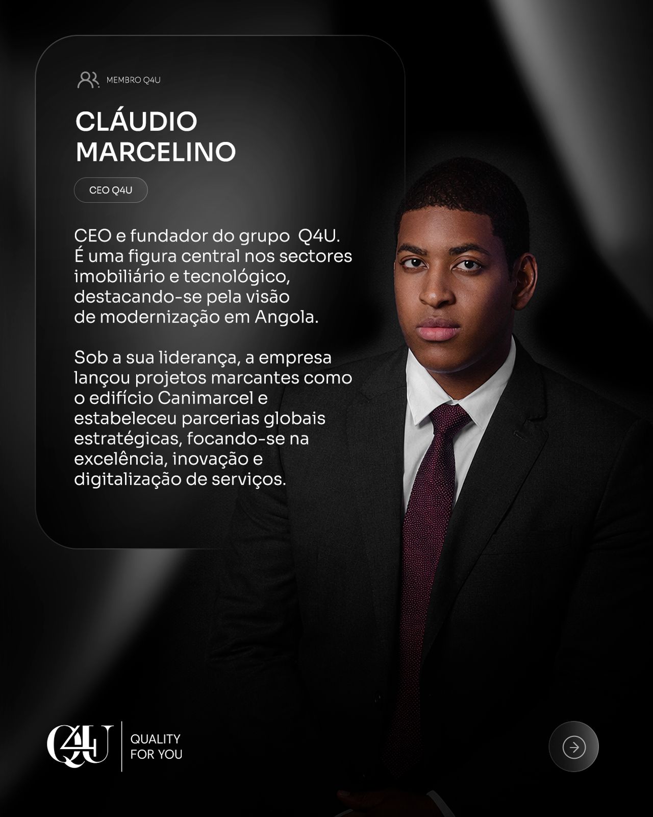 Man with a bald head, beard, and glasses, wearing a blue suit and white shirt, stands confidently against a white, ornate wall. Professional and composed.