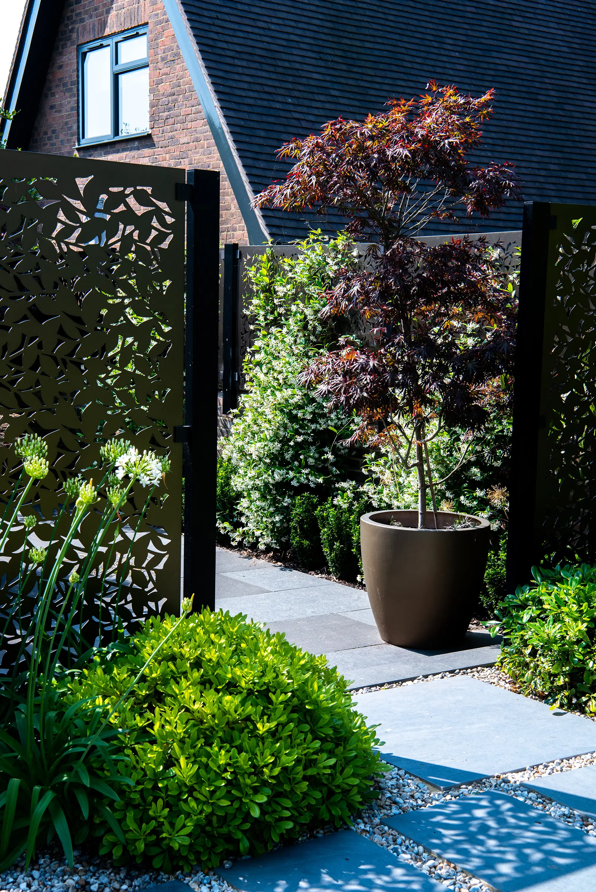 A tranquil garden pathway leads to a house, framed by lush greenery and decorative plants.