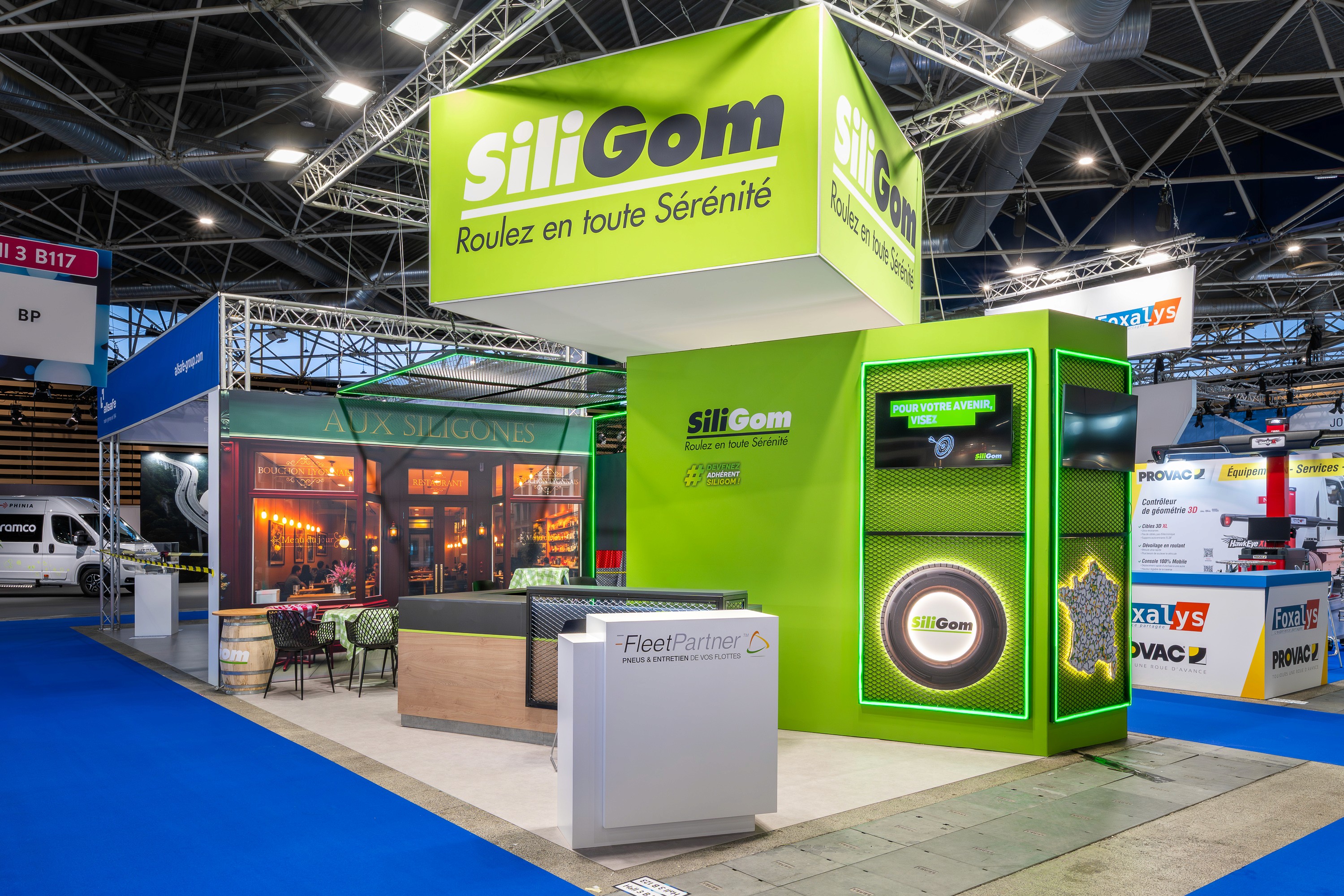 Stand SiliGom Solutrans Lyon 2026 réalisé par Expace – vue frontale du stand avec façades vert intense, logo Built to last longer en hauteur et présentoir produit circulaire central