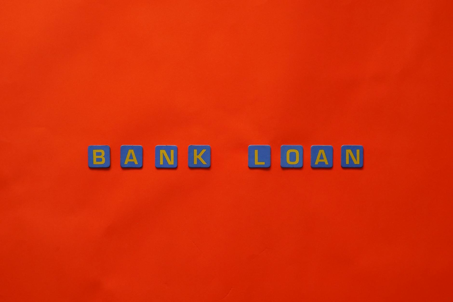 Blue letter tiles spelling BANK LOAN arranged on a bright red background