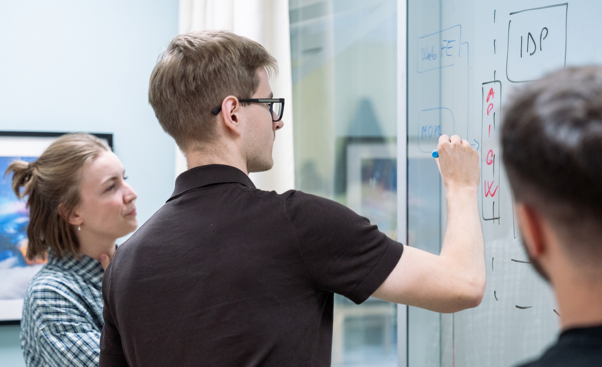 Solution architect sketching a system diagram with API gateway and IDP boxes on a glass whiteboard