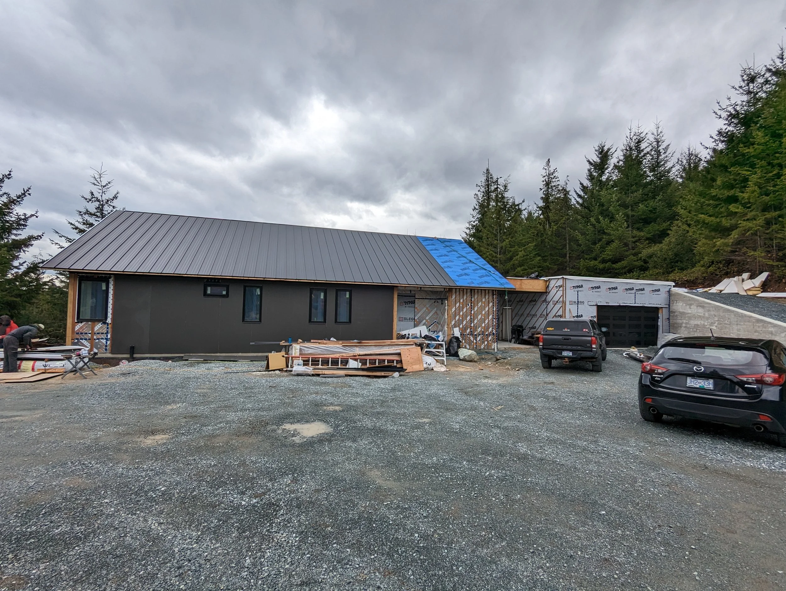 Modern two-story home with large glass windows, warmly lit interiors, and a balcony. Surrounded by trees and a manicured lawn at dusk. Cozy ambiance.