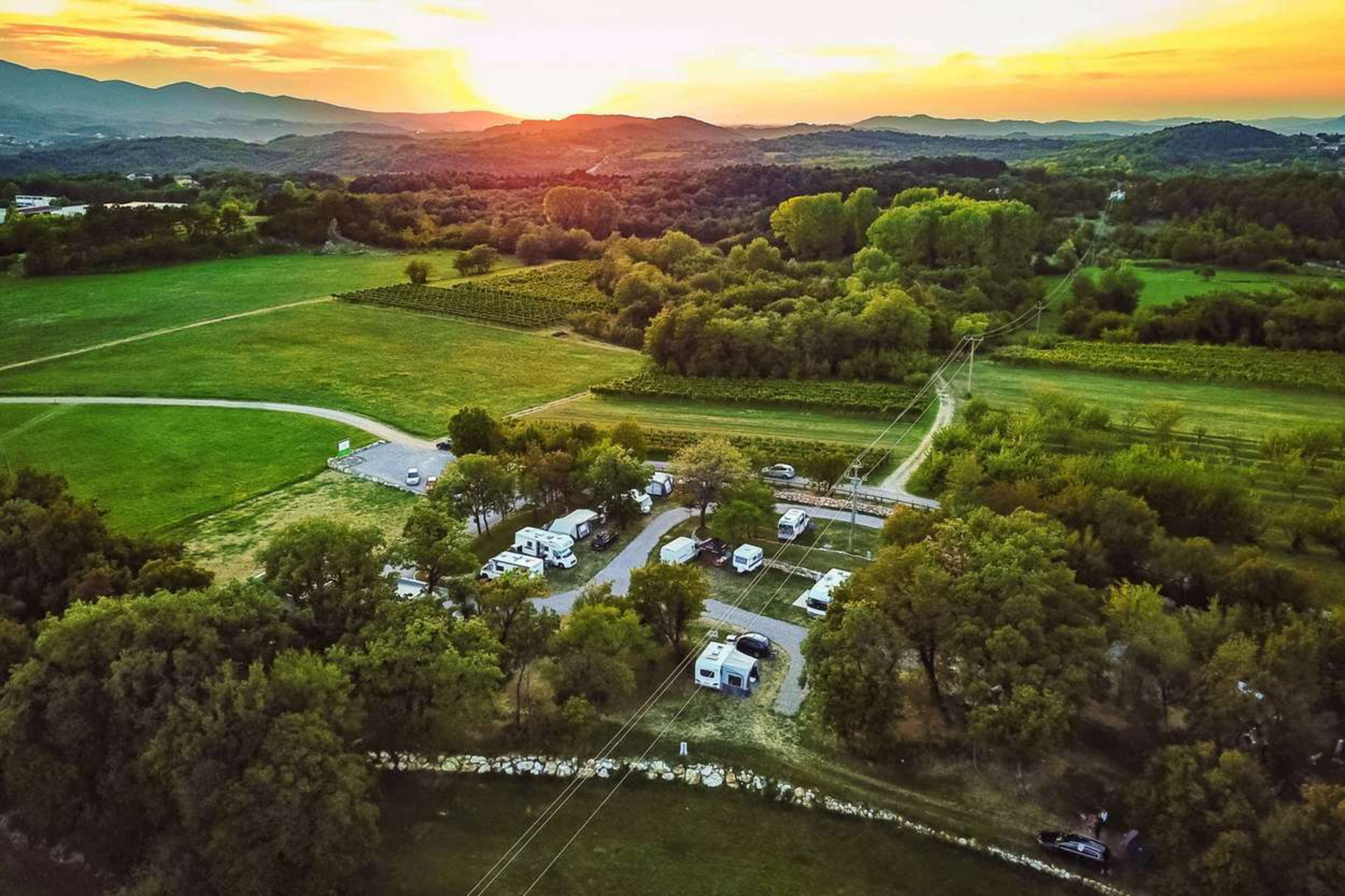 The sun sets behind a small RV campground in a lush valley with trees and grassy fields..