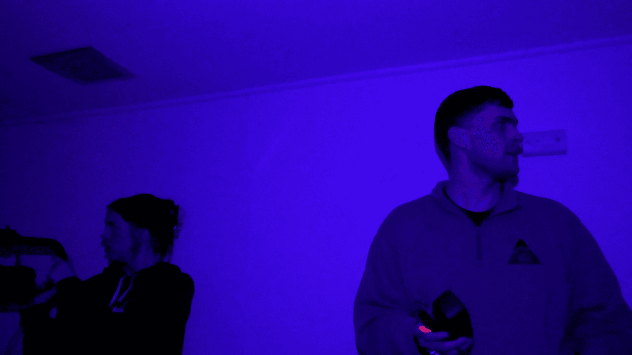 Paranormal investigation team scans a room under purple lighting while conducting real-time field research.