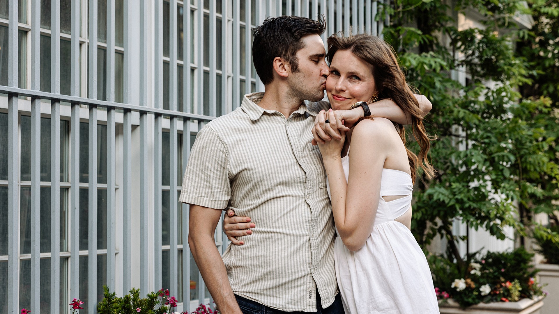 Newly engaged couple in an intimate close-up at the cobblestoned Washington Mews in Greenwich Village, NYC — he's kissing her while she glows at the camera — romantic engagement photography by Lizz Spano Photography, New York City engagement photographer.