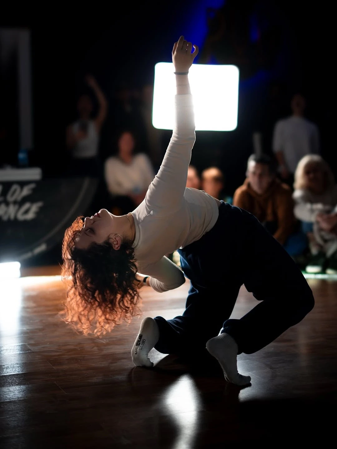 A group of dancers practicing in a spacious studio with wooden floors and large windows.