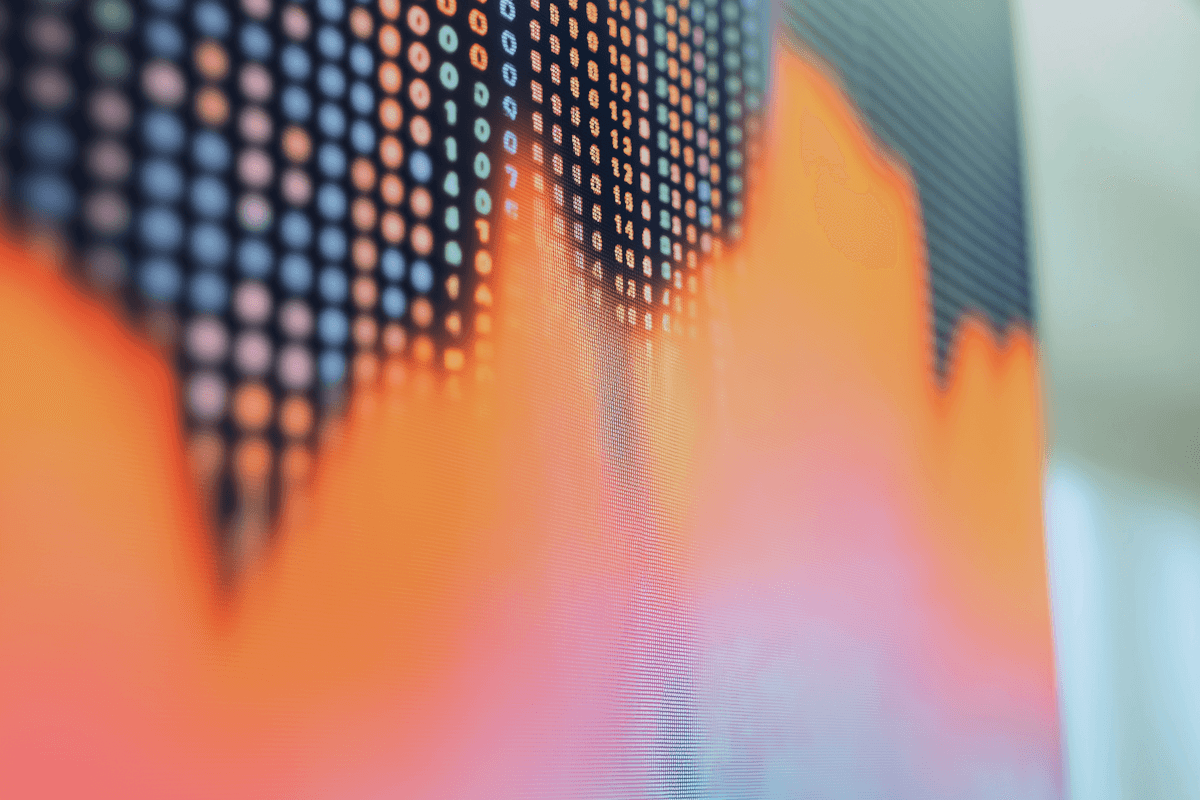 A person holding a report showing a blue bar graph, indicating growth, while seated at a desk with a laptop.