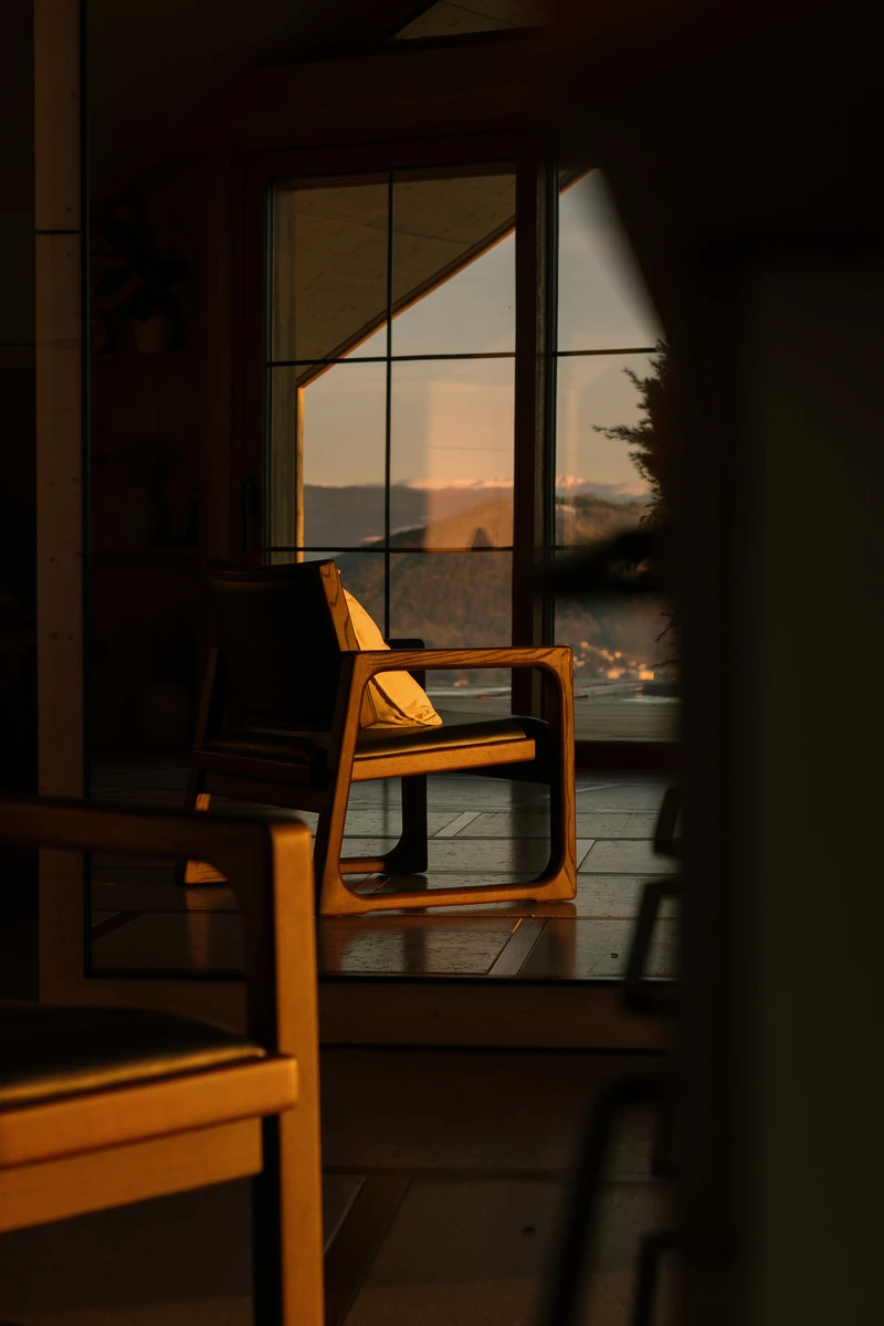 Holzsessel vor dem Fenster im Abendlicht, dahinter die dämmrige Hügellandschaft