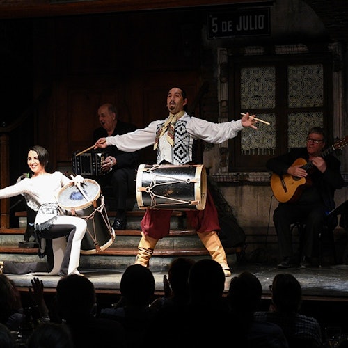 Artistas en el escenario: un hombre y una mujer tocando la batería, otro hombre tocando un acordeón, y un cuarto hombre tocando una guitarra.