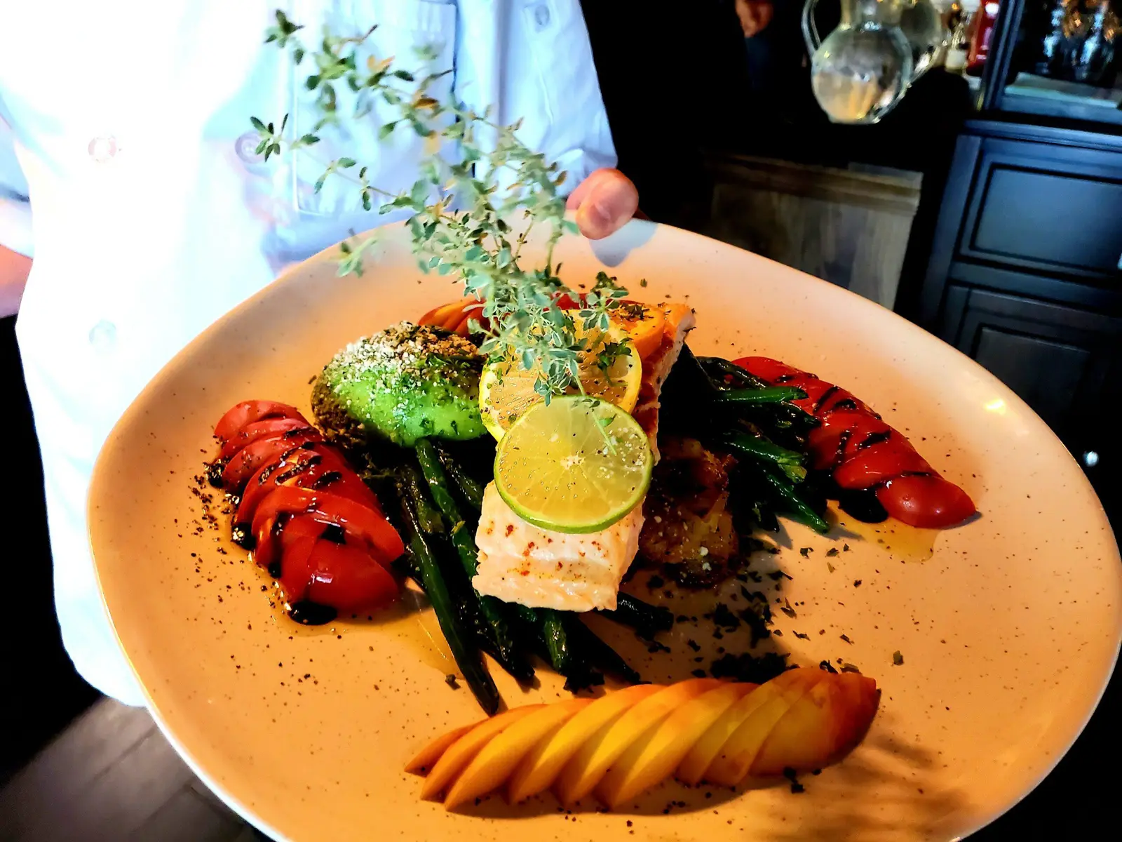 Gourmet salmon dish with avocado, asparagus, tomatoes, and lime.