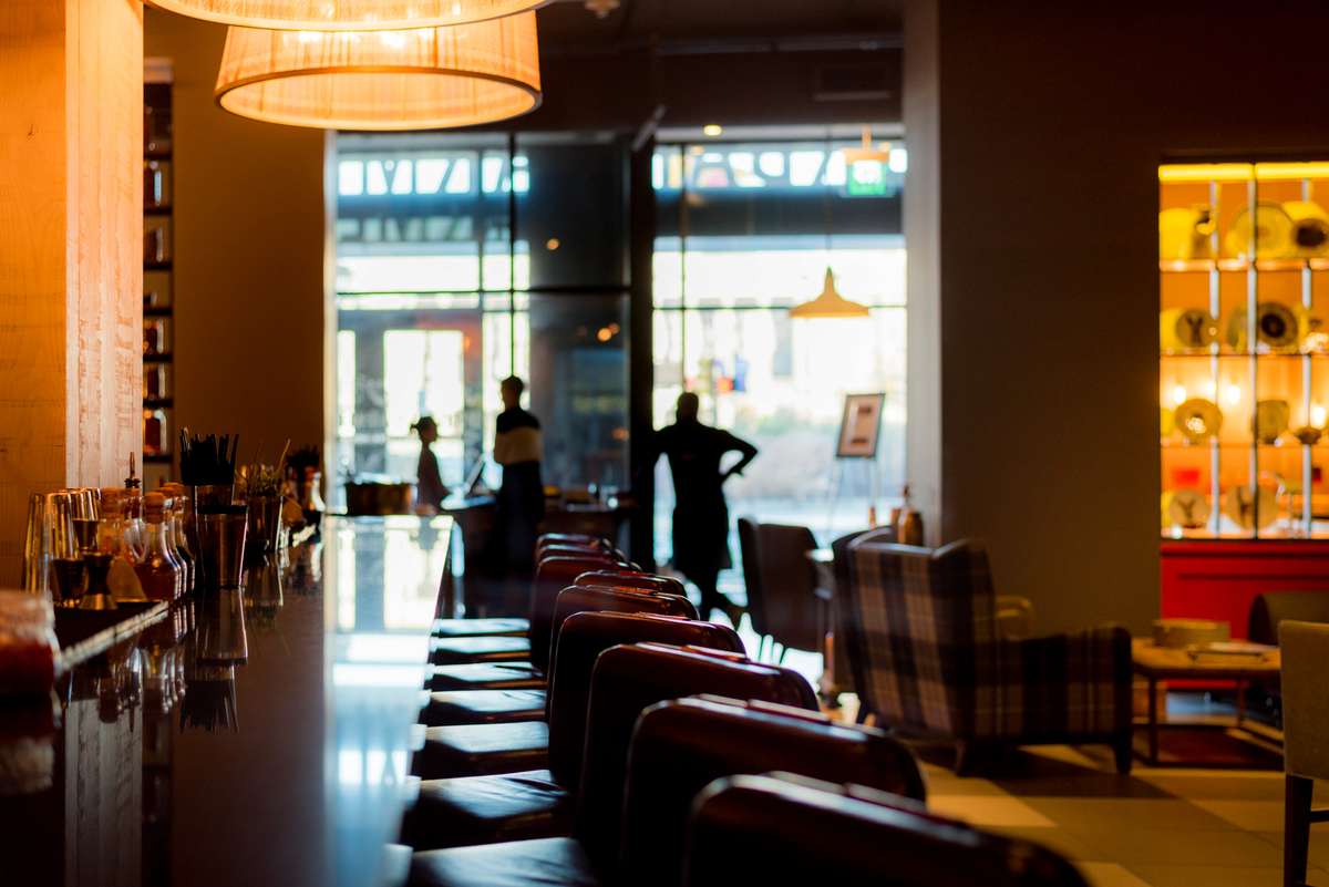 A modern lounge with rows of red and black leather armchairs facing a large window overlooking a city street at dusk.