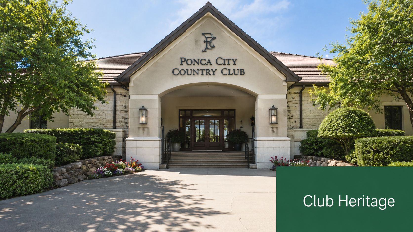 The entrance to the Ponca City Country Club featuring a stone facade, a peaked roof, and lush landscaping.