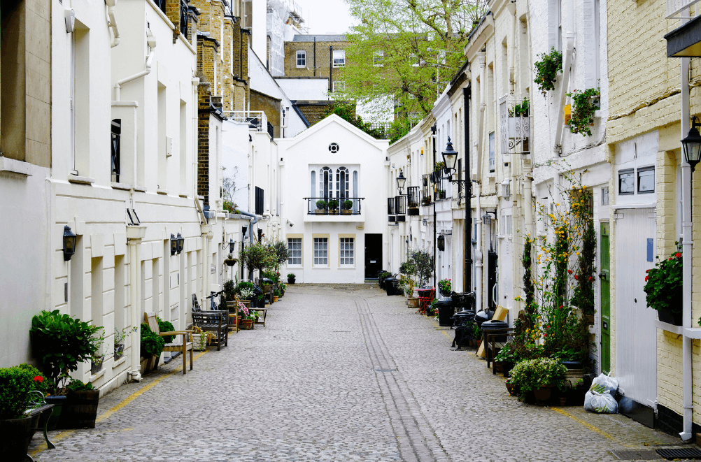 A serene outdoor seating area with two chairs, surrounded by lush greenery and a glassed-in structure.
