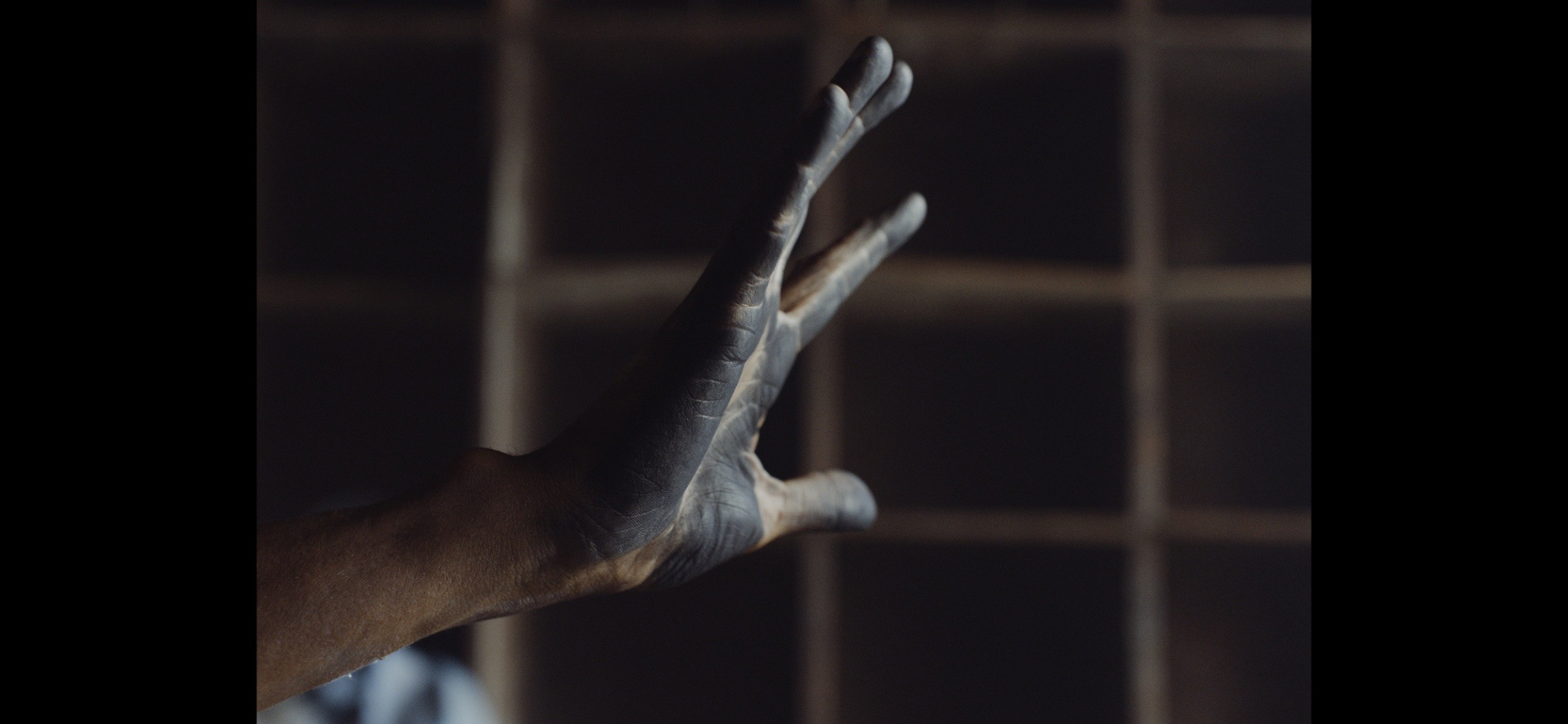 A close-up of a hand with black pastel smears, slightly splayed, extending towards the light.