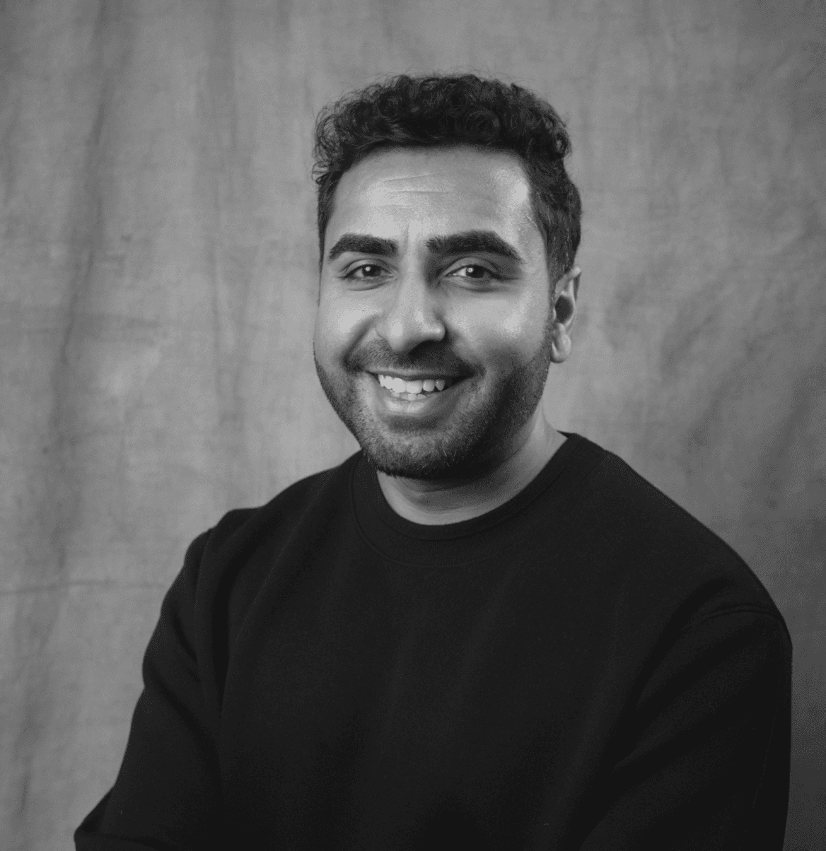 Black and white portrait of a smiling bearded team member in a dark sweater