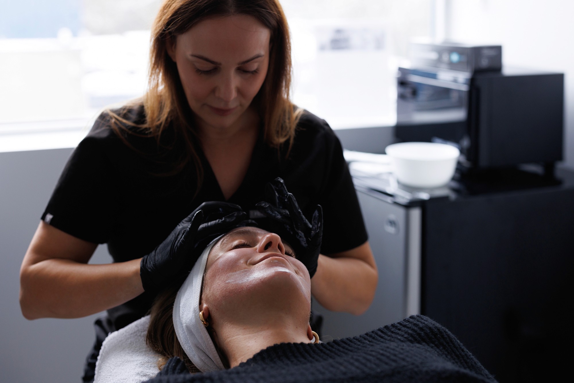 Patiente lors d'un traitement de microneedling. Couchée surl e dos avec l'esthéticienne ayant les mains sur son visage.