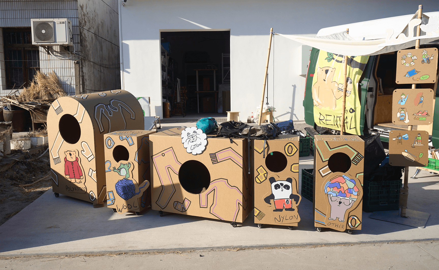 Cardboard recycling bins for Polyester, Wool, Cotton, Nylon, and Other clothing, featuring custom illustrations.