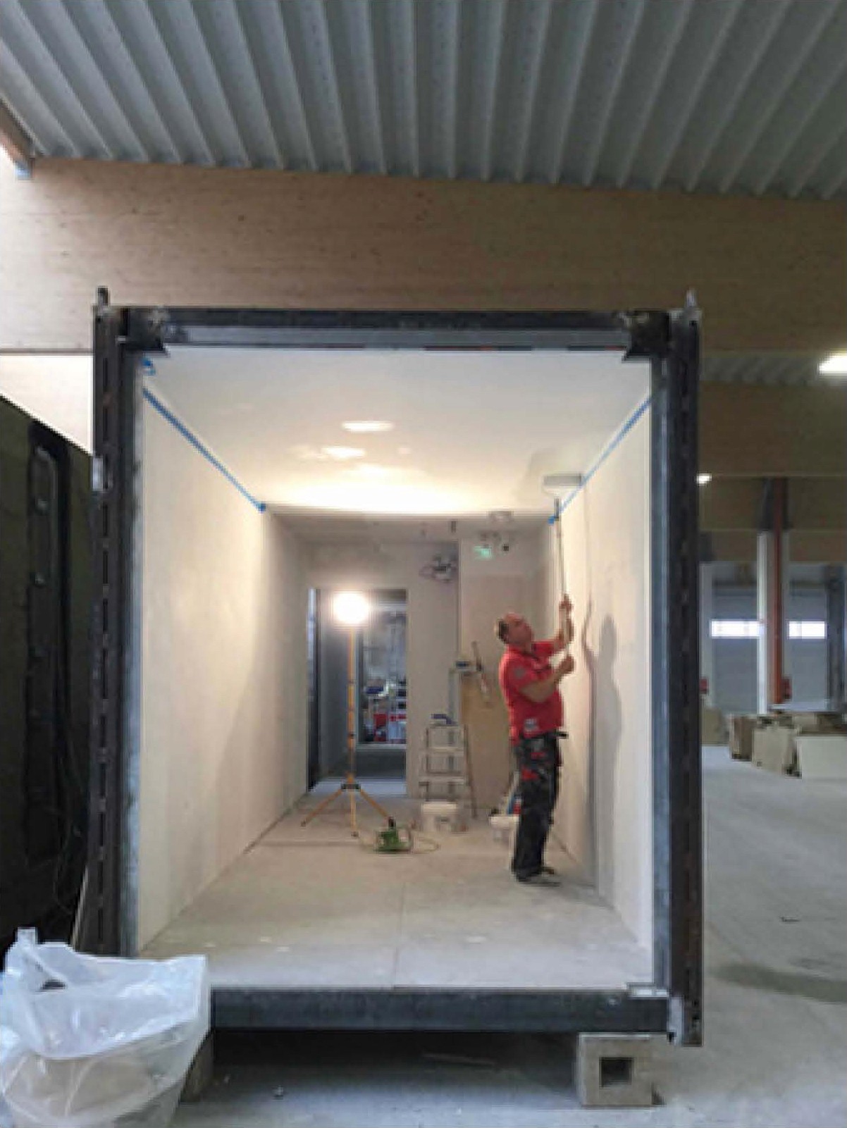 A worker meticulously paints the interior of a bare guestroom module inside a factory in China.