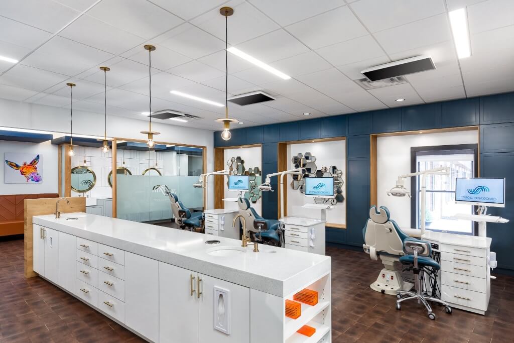 Modern orthodontist interior featuring white cabinetry, desks, and large windows, with a polished wooden floor.